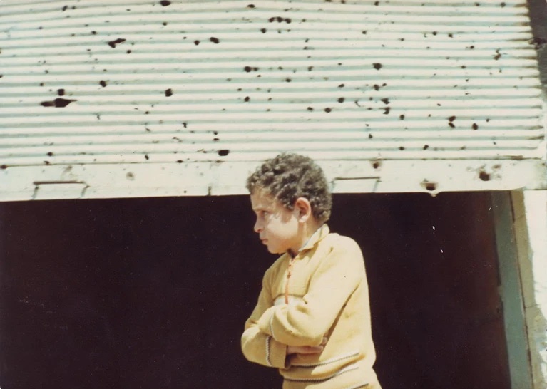 صبي صغير يقف أمام متجر في أعقاب مجزرة حماة التي وقعت في سوريا عام 1982، ومن ورائه يظهر باب المتجر وقد ملأته الثقوب التي خلَّفها إطلاق الرصاص.
